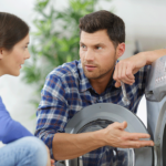 Junger Mann und junge Frau hocken vor einer Waschmaschine