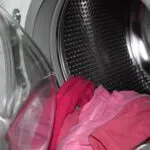 Rosane Sachen hängen aus einer gebrauchten Waschmaschine