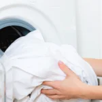Junge Frau holt nicht ganz trockene Handtücher aus einem Wäschetrockner